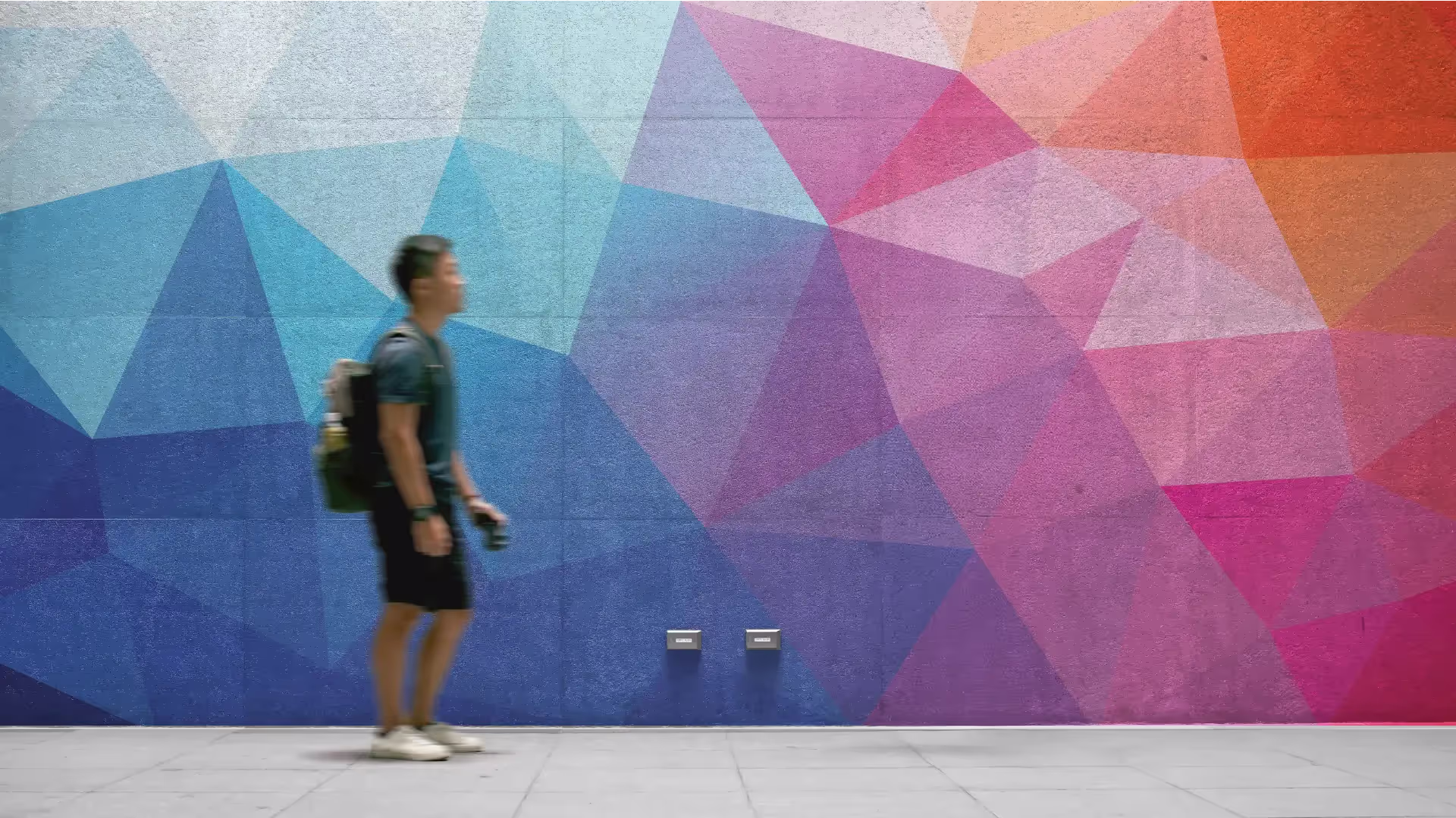 Man walking in front of a painted wall. The design on the wall is of a Polygon gradient