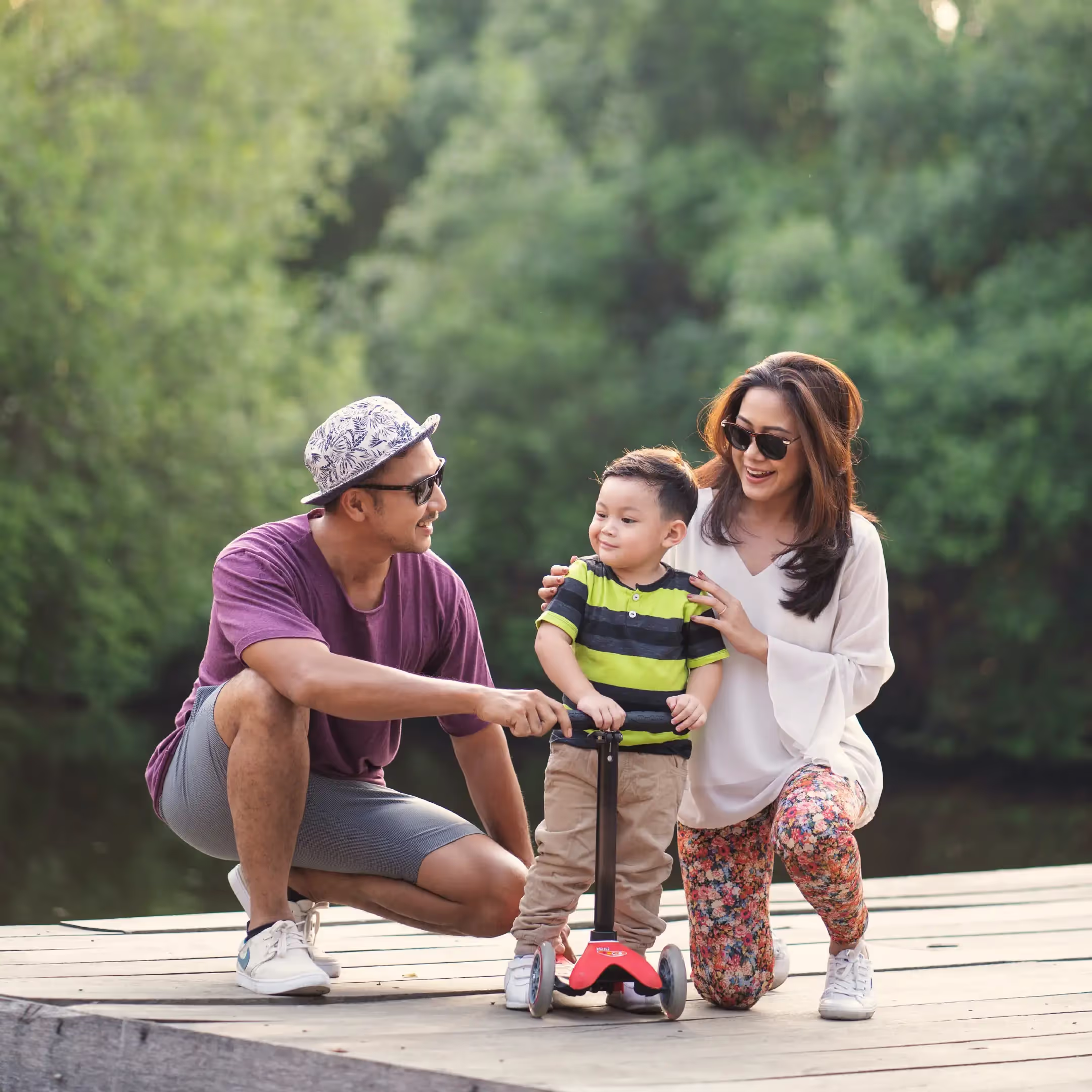 A millenial heterosexual couple sitting on a lakefront dock with their toddler son.