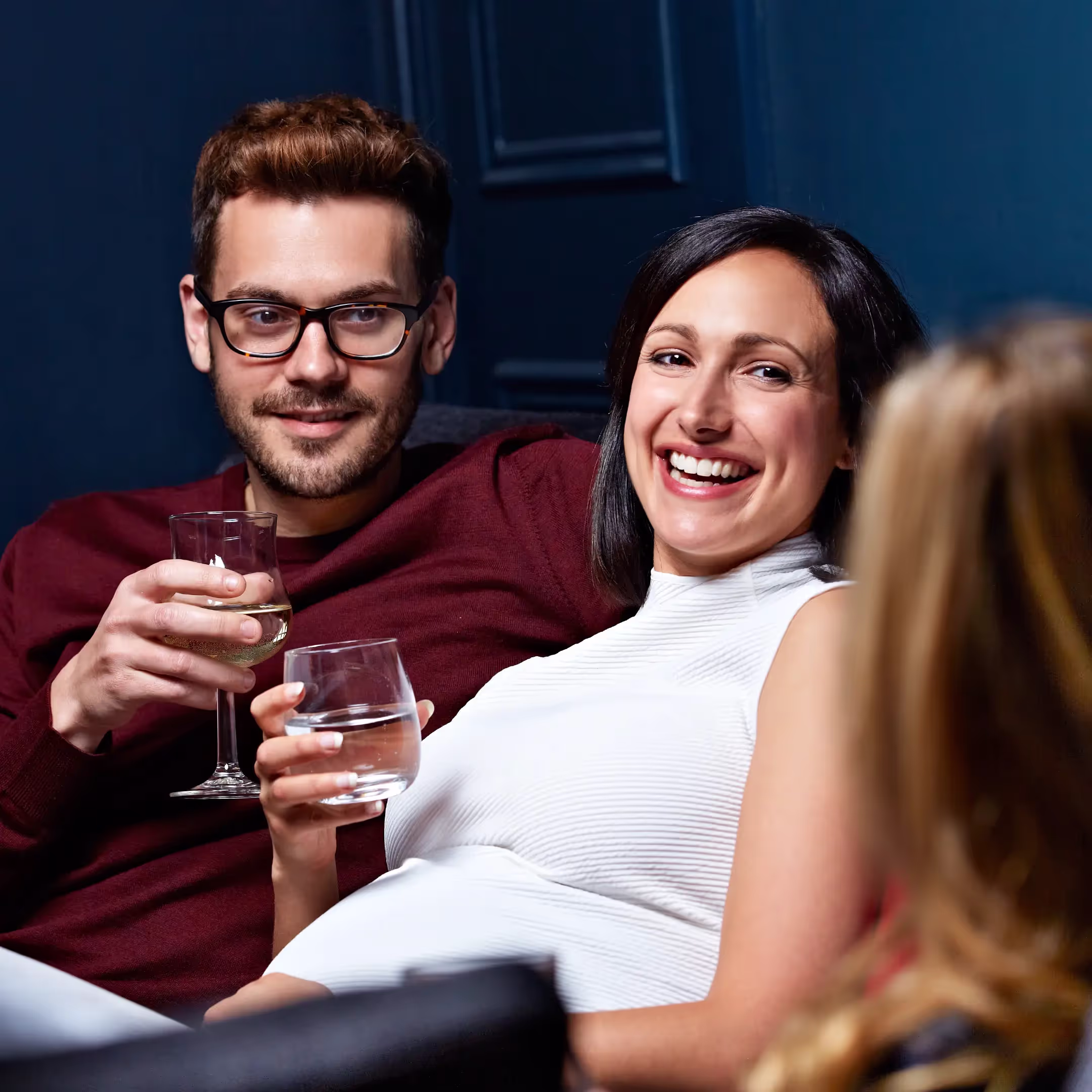 three people sitting down having a conversation. two are drinking wine, one is drinking water.